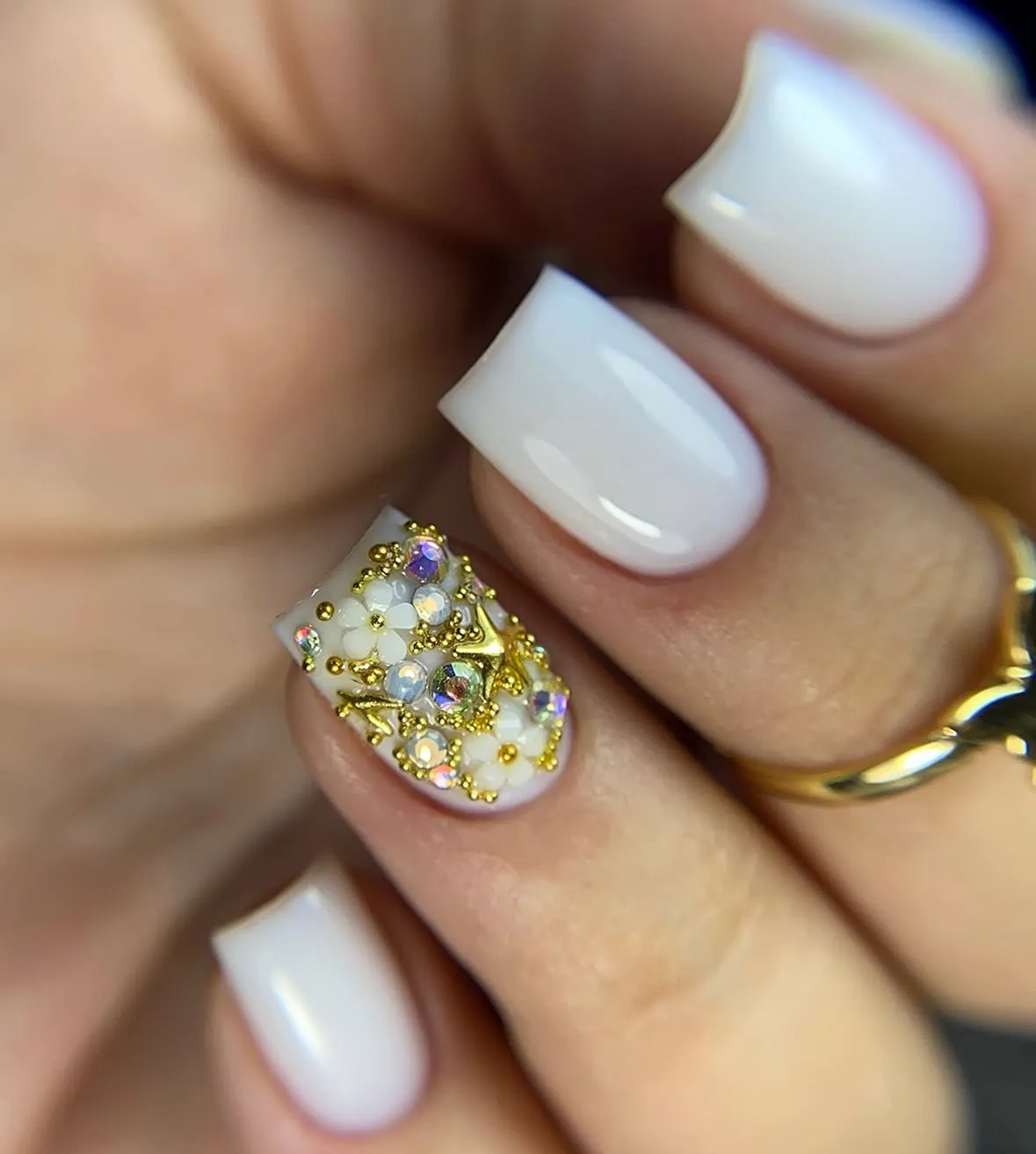 Uñas cortas en blanco lechoso con una uña decorada con flores, cristales y detalles dorados